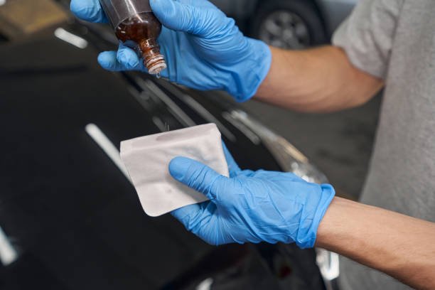 Close up of hands in blue protective gloves carefully applies special fluid on cloth during car detailing