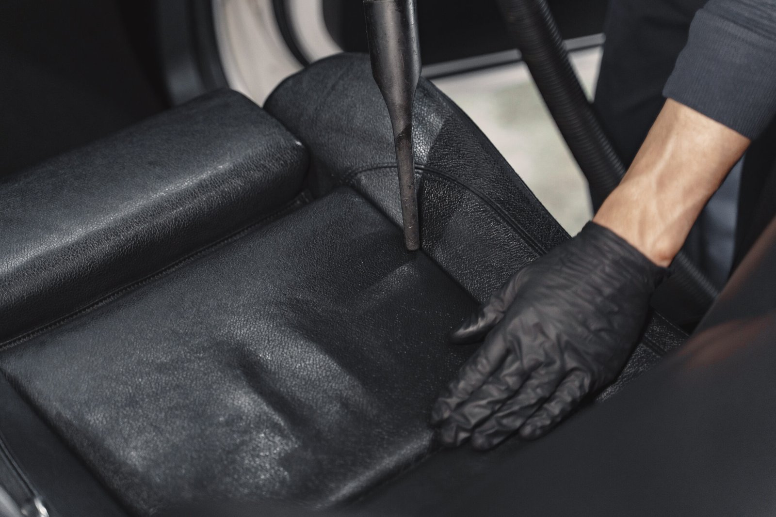 Man cleaning his car with vacuum cleaner. Man in a black uniform.